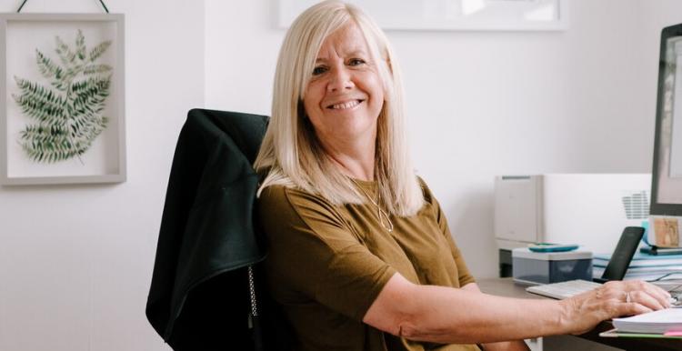 A woman sits at her desk and smiles at the camera