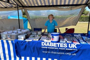 A woman wearing a blue t shirt standing outside in front of a stall with leaflets and books. A Diabetes UK blue banner is in the foreground.