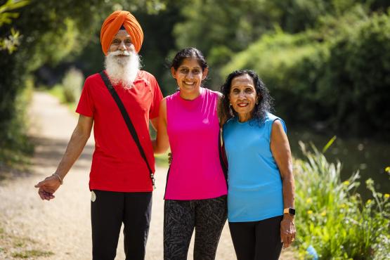 A man and two women stand together surrounded by greenery. They are all wearing bright colours and the sun is shining.