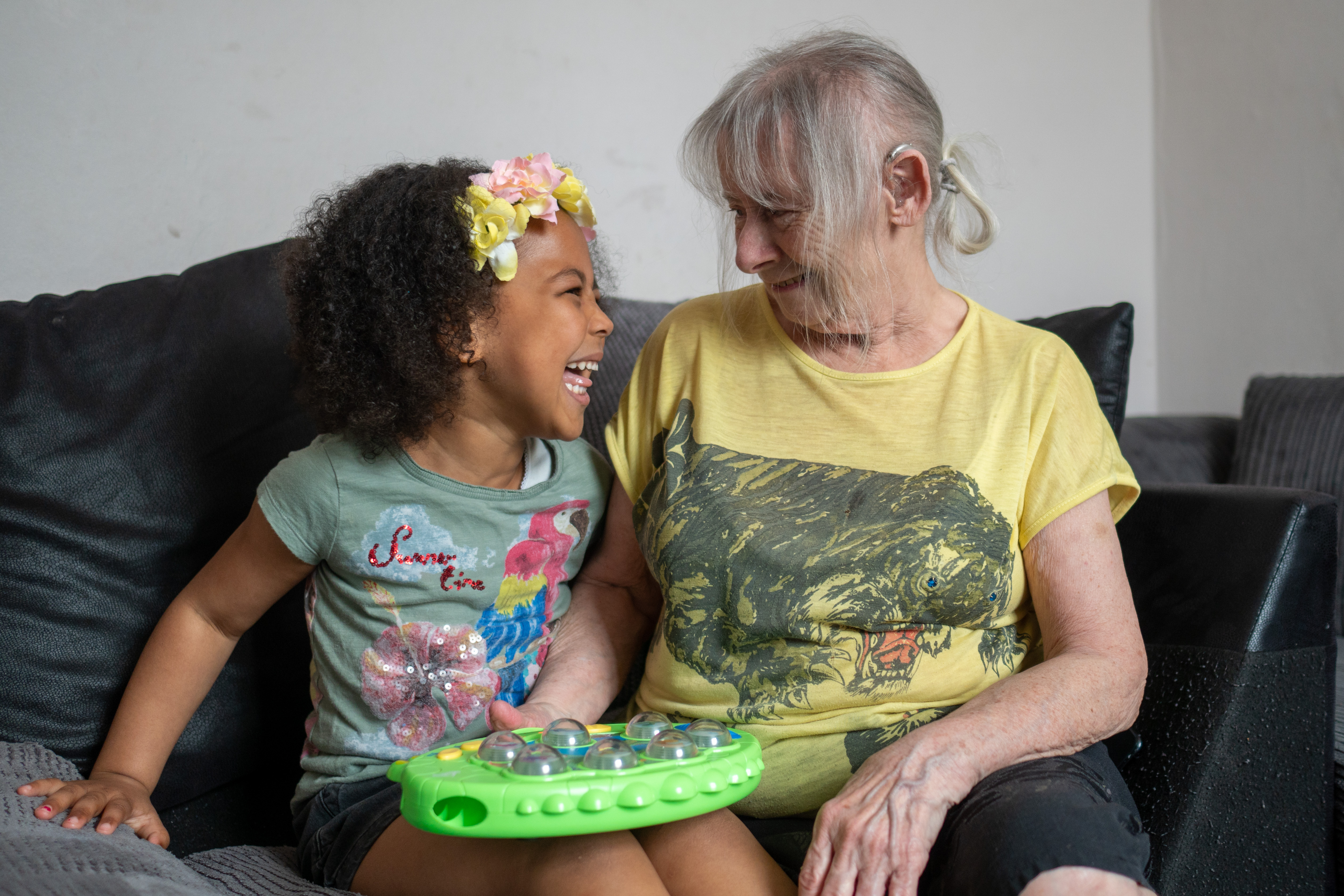 A young girl sitting next to an older woman on a sofa smiling at each other