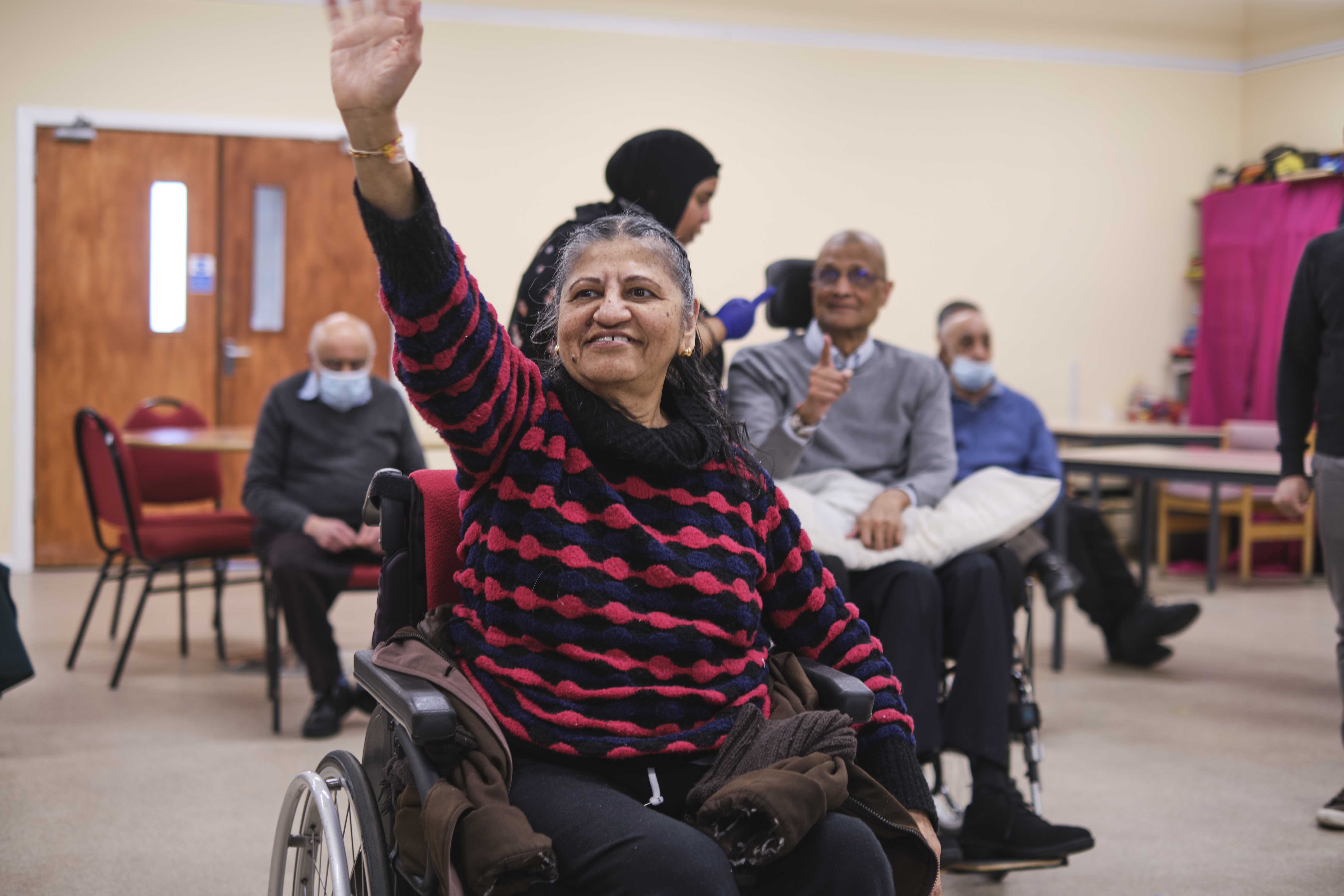 A woman in a wheelchair with her arms up and smiling 