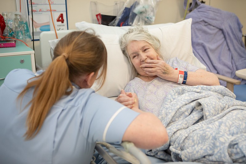 A nurse holding an elderly patients hand 