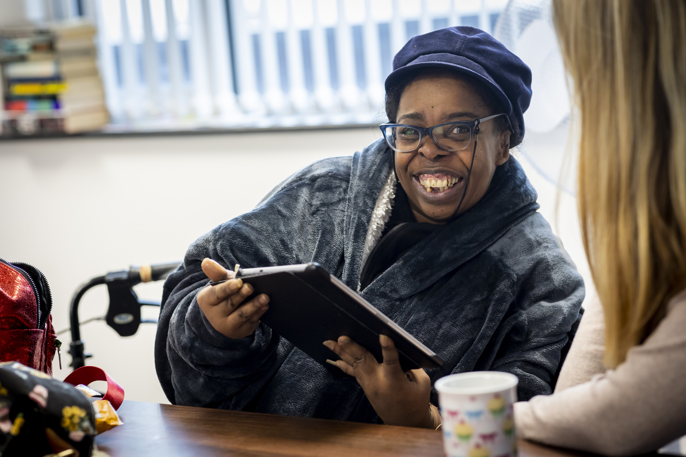 A woman wearing a hat smiling and an ipad