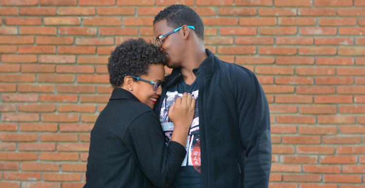 A man and woman standing in front of a brick wall hugging 