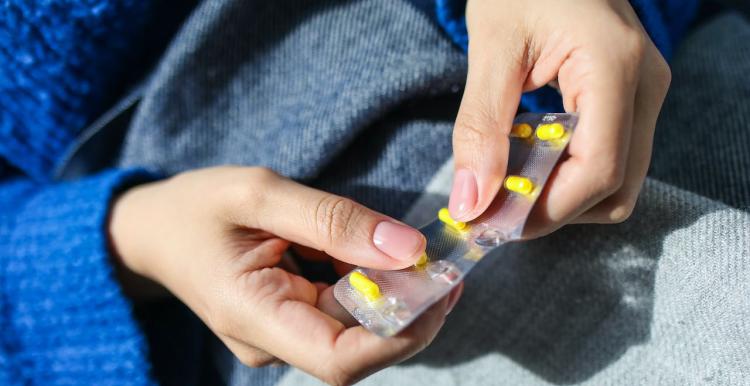A close up of someone holding yellow pills in their hands, wearing a bright blue jumper 
