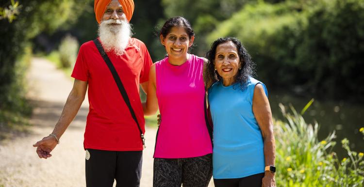 A man and two women stand together surrounded by greenery. They are all wearing bright colours and the sun is shining.