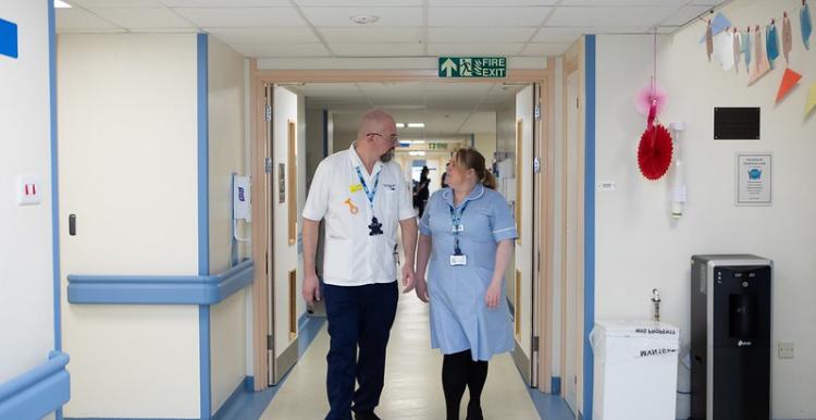 A man and a woman in hospital uniform walking along a hospital corridor 