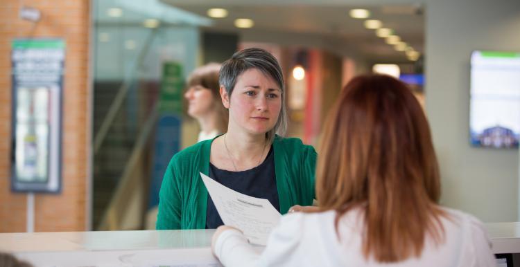 A woman with short hair and a green cardigan standing at a doctor's reception desk