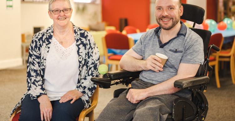 A woman sitting next to a man in a wheelchair, both are smiling 