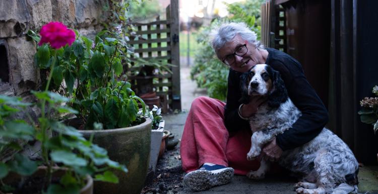 An elderly woman sits outside with her dog 