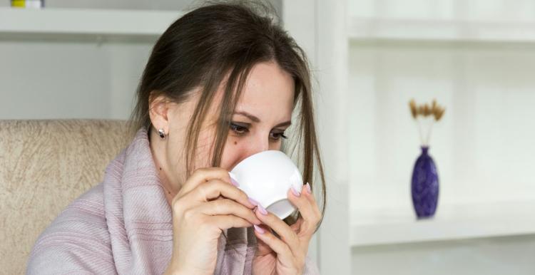 A woman wrapped in a blanket holding a hot drink in a mug