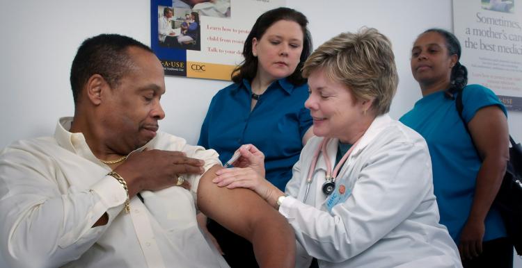 A man having a vaccination, and two people queuing behind him.