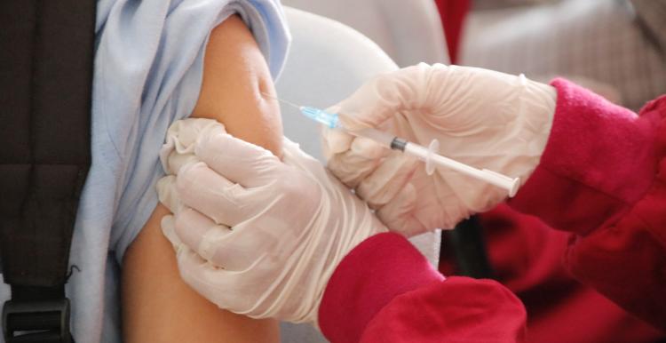 A close up of an arm with a vaccination needle in it. The person holding the needle is wearing surgical gloves. 