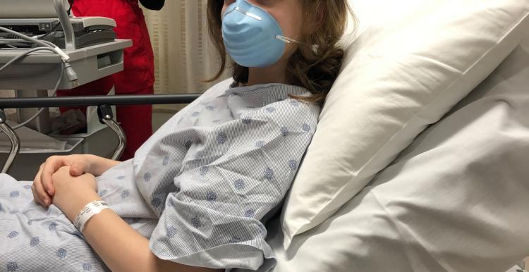 A patient in a hospital bed wearing a mask