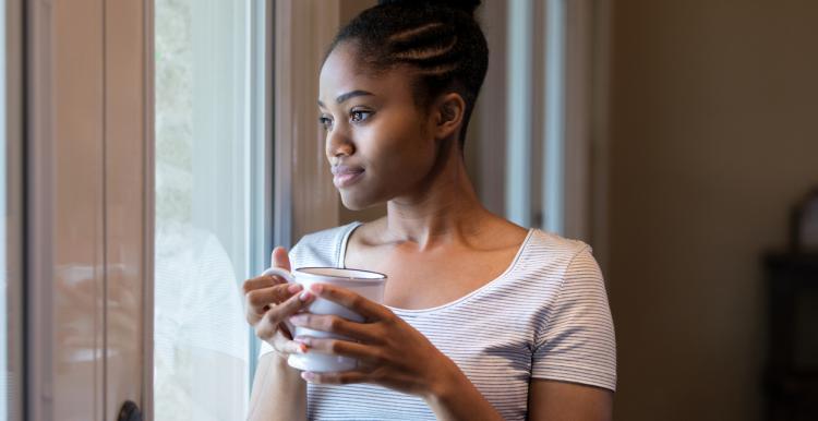 A woman stands next to a window holding a mug 