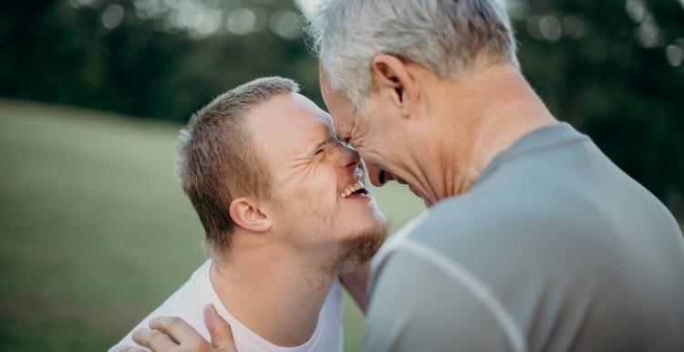 A boy with Downs Syndrome hugging an older relative and smiling 