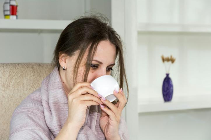 A woman wrapped in a blanket holding a hot drink in a mug