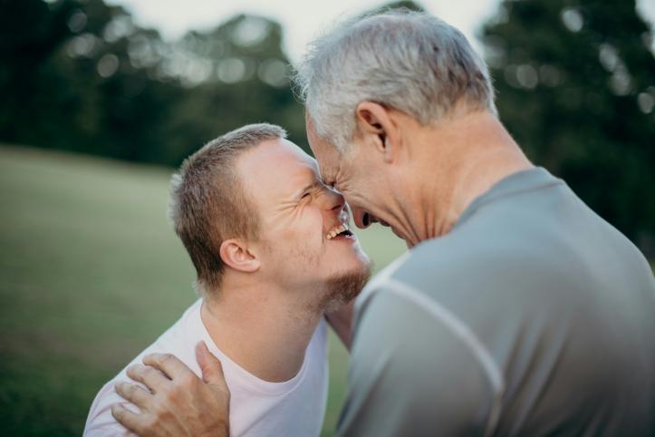 A boy with Downs Syndrome hugging an older relative and smiling 