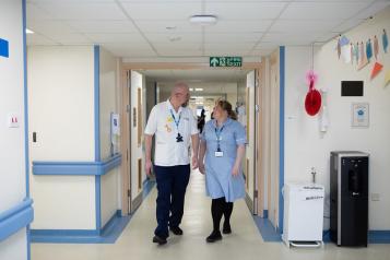 A man and a woman in hospital uniform walking along a hospital corridor 