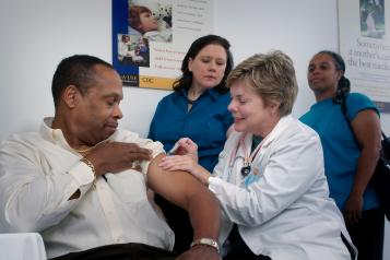 A man having a vaccination, and two people queuing behind him.