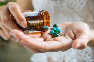 Hands holding a medicine bottle with green pills