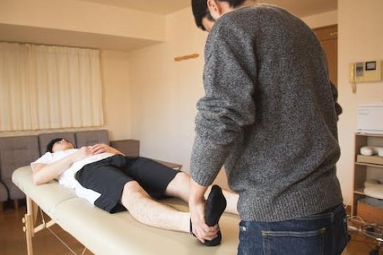 A man on a physio table, with a physio wearing a grey jumper holding his foot