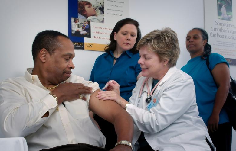 A man having a vaccination, and two people queuing behind him.